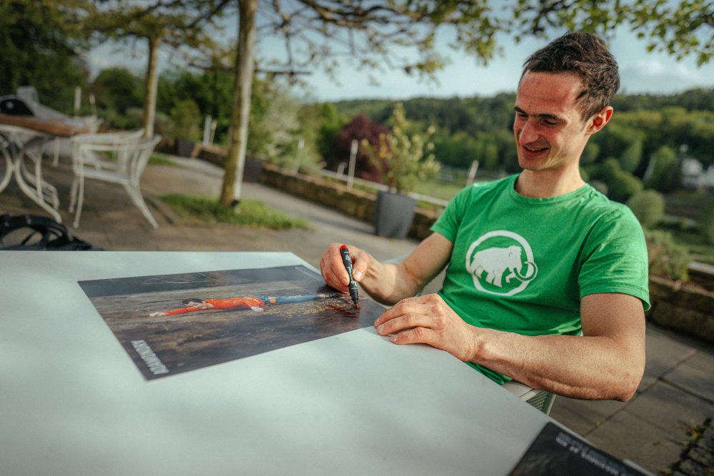 Adam Ondra sitting behind the table and signing his poster