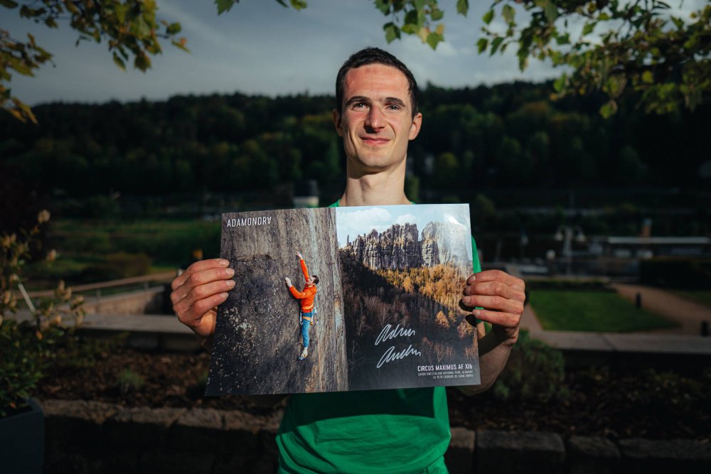 Adam Ondra posing with his Circus Maximus poster, landscape version