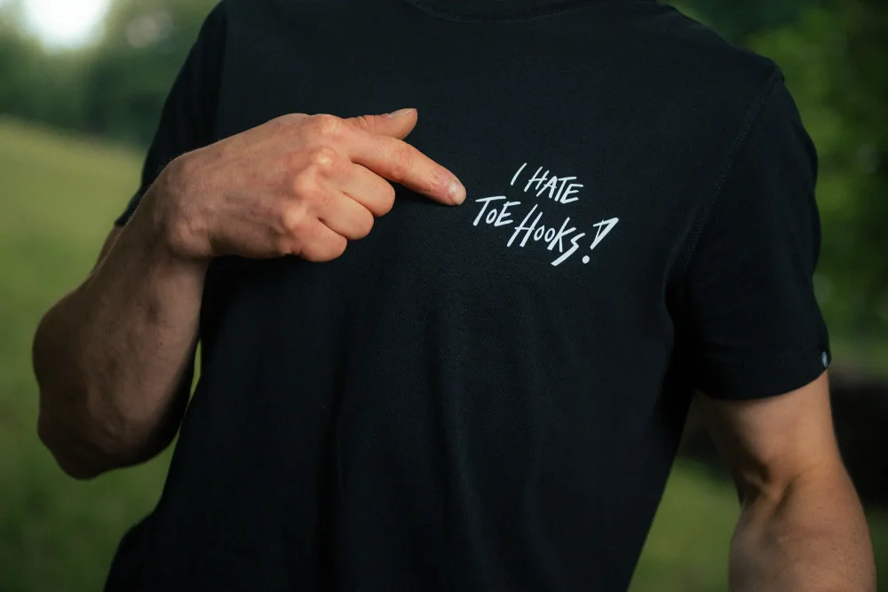 A model pointing at the "I hate toehooks" sign on the front side of AO black T-shirt