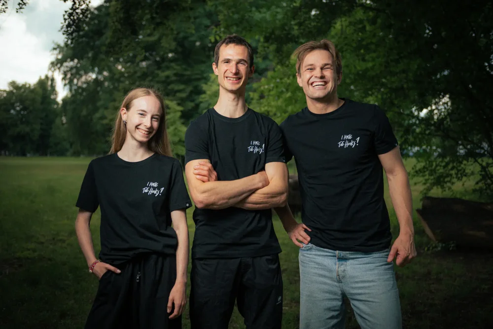 Adam Ondra and two models posing in the AO "I hate toehooks" black T-shirt, front side