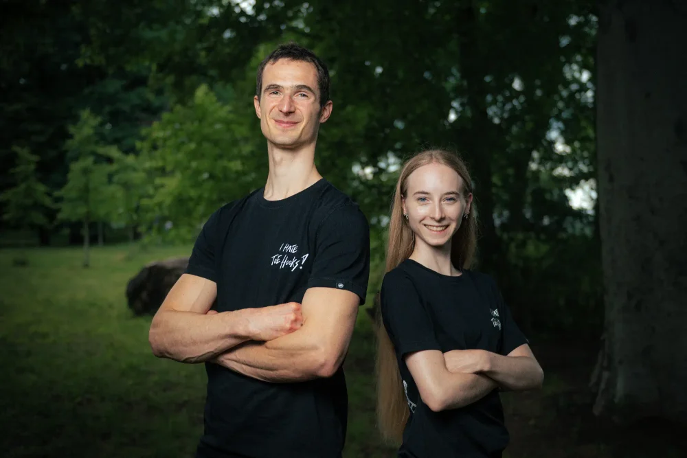 Adam Ondra and a woman model posing in the AO "I hate toehooks" black T-shirt, front side